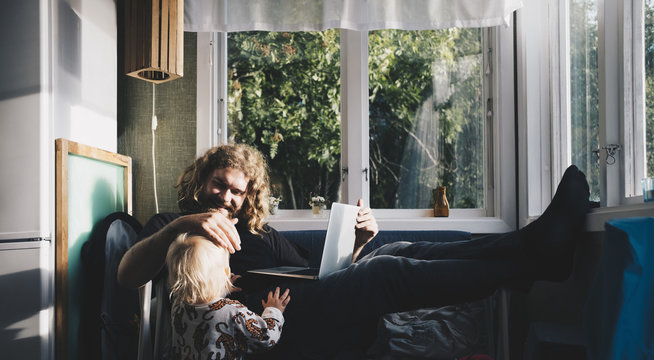 Father using laptop and talking to baby daughter