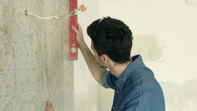 Young man checking wall with level at new home 
