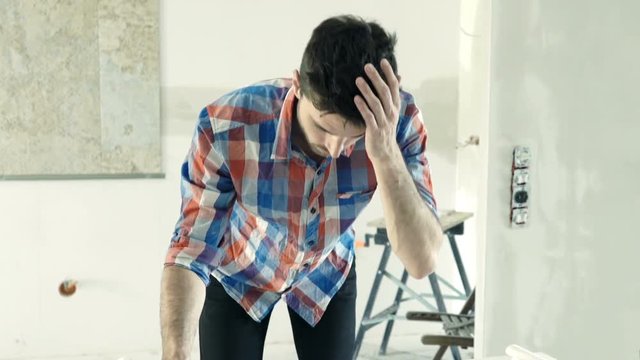 Unhappy, overwhelmed man working with blueprints at his new home
