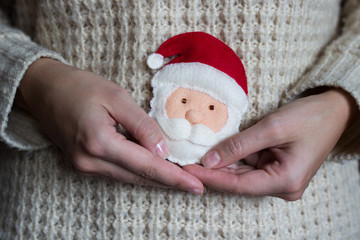 A woman is holding a toy for a Christmas tree, a handmade. Santa Claus symbol.
