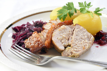 Roast pork with potatoes, red cabbage and cranberries on a white plate with a fork