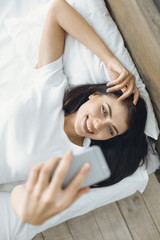 Warm bed. Attractive female person expressing positivity and raising hand while looking at telephone