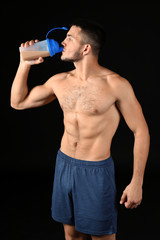 Handsome young man drinking protein shake on black background