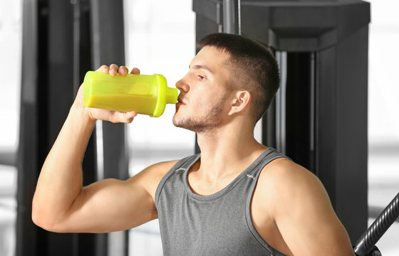 Handsome young man drinking protein shake in gym