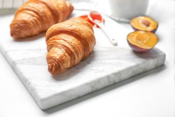 Board with delicious croissants on white background