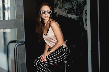 Young and beautiful girl in a beige t-shirt and black breeches in a white stripe. Women's fashion. Urban way of life