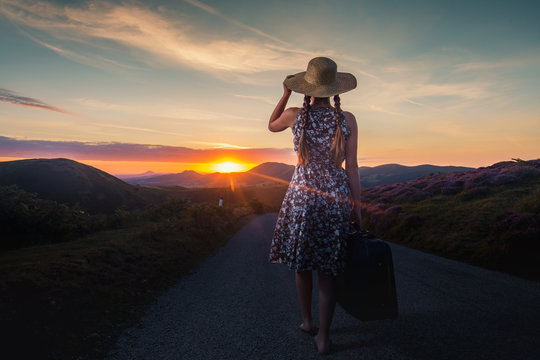 Girl with a Hat Carrying a Suitcase at the Top of Scenic Mountain at Sunrise