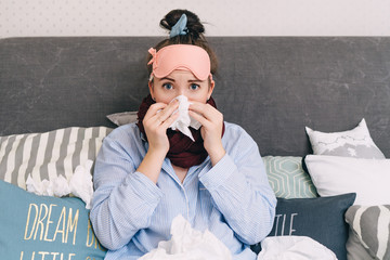 Young sick woman in bed with flu and cold blowing her nose
