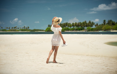 Girl in hat and white dress on the beach. On the shore of the ocean. Maldives, the island. Vacation, travel.
