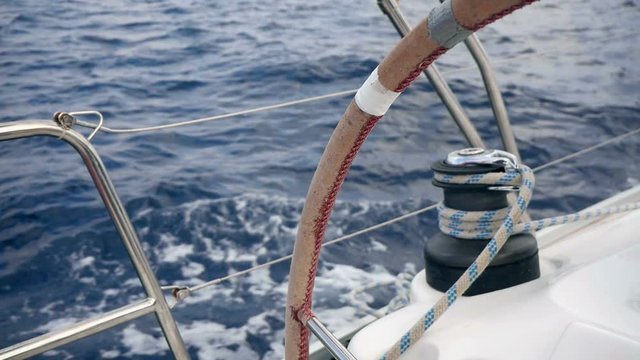 Closeup on left sailing boats winch looking through steering wheel turning round. Filmed on moving sailing boat with waves splashing from side of boat in slow motion hd.