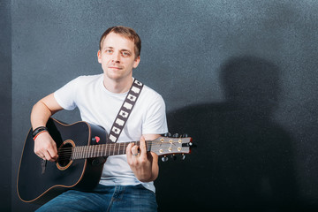 Cheerful guitarist. Cheerful handsome young man playing guitar and smiling while sitting at chair