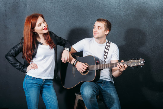 Portrait of young multiracial couple of man playing bass guitar and dancer girl on gray
