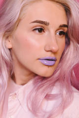 A studio portrait of beautiful young girl with lilac hair posing over purple wall. Stylish and sensual female model with violet lips wearing trendy pink clothes