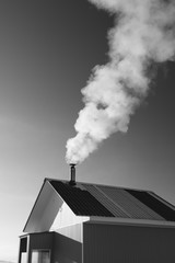 The smoke from the chimney of a small frame house, black and white.