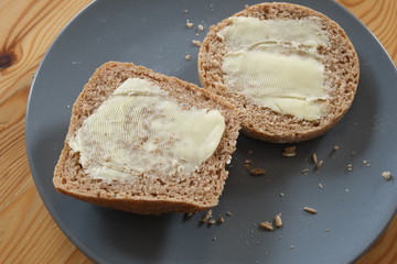 Zwei halbe Brötchen auf einem Teller, mit Butter bestrichen.