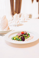 Leaf salad with kiwi, pineapple and veal medallions served on white plate. Delicious restaurant food