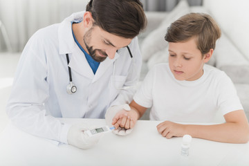 Obraz premium The doctor takes the blood from the boy with a finger using a scarifier. The boy staunchly endures the procedure.