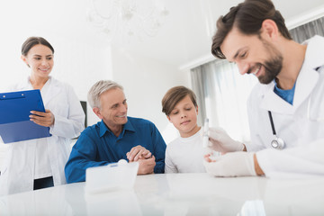 Fototapeta premium The doctor in white medical gloves takes the boy's blood sample to the level of sugar. Nearby is the boy's grandfather.