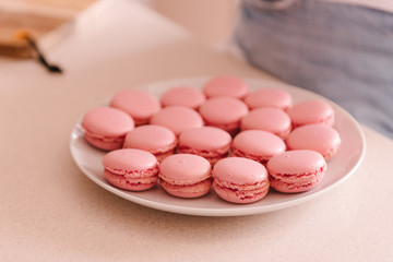 Close up pink sweet macaroons on white plate. French tasty cookies, dessert. The result of cooking, homemade food, kitchen