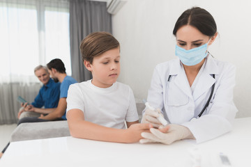 Obraz premium A nurse takes a blood test with a boy's scarifier. A nurse is sitting in a mask and gloves at the table.