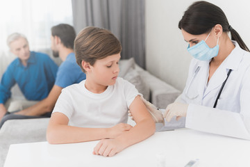 The nurse makes an insulin injection to the boy. A nurse is sitting in a mask and gloves at the table.