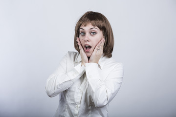 ragazza con capelli a caschetto e camicia bianca, guarda in macchina e si stupisce con le mani in...