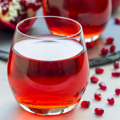 Pomegranate drink in glass and fruit on background, closeup, square