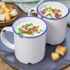 Creamy potato soup garnished with bacon and green onion, served in mug, square