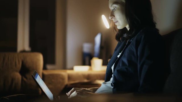 Young concentrated woman working at home in night time using laptop computer and typing message
