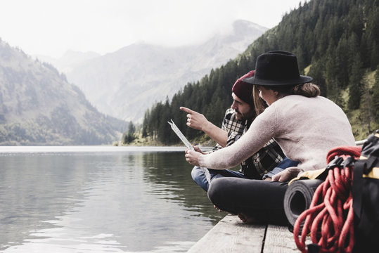 Austria, Tyrol, Alps, couple with map sitting on jetty at mountain lake