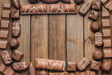 A frame of chocolate candies and bars on a wooden background, free space for text