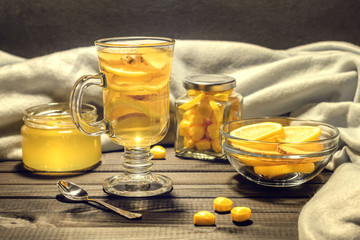 Tea with ginger and lemon in a glass cup and yellow sweets on a wooden background close up
