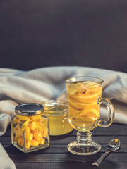 Tea with ginger and lemon in a glass cup and yellow sweets on a wooden background close up