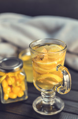 Tea with ginger and lemon in a glass cup and yellow sweets on a wooden background close up