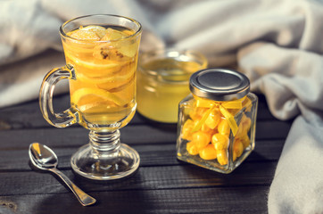 Tea with ginger and lemon in a glass cup and yellow sweets on a wooden background close up
