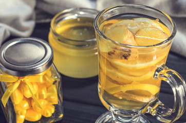 Tea with ginger and lemon in a glass cup and yellow sweets on a wooden background close up