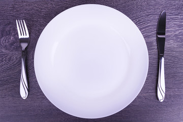 Empty plate, fork and knife isolated on wooden table.