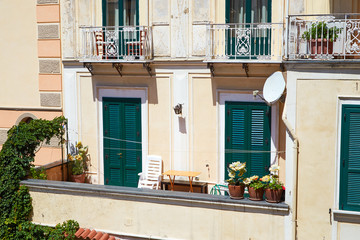 Typical Italian balcony of the resort city with sun loungers, flowers and closed green shutters. Amalfi, Italy.