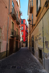 A narrow Italian street with shabby walls and a fragment of a bright house with red walls in the distance. City of Salerno, Italy