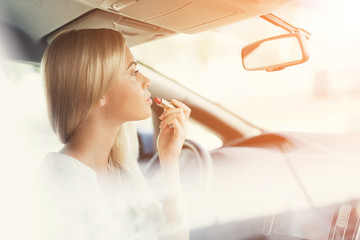 A young girl paints her lips while sitting at the wheel of an electric car.