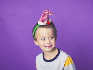young 5 year old boy with christmas decoration on his head in front of violet background