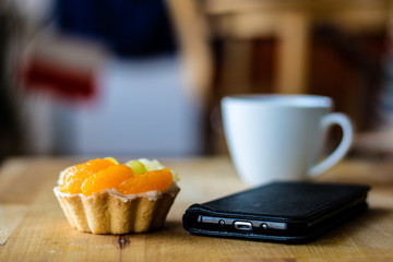 Tasty muffin with fruit on a wooden kitchen table. Coffee and phone with notes.
