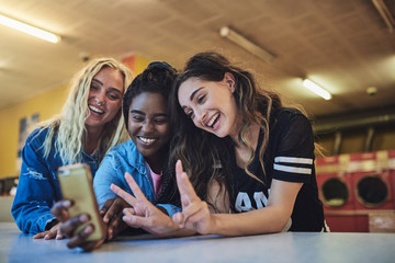 Smiling friends hanging out in a laundromat taking selfies together