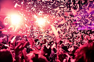 Confetti fired in the air during a in a disco. Hundreds of hands to the sky. Purple, magenta an pink tone/background with high contrast