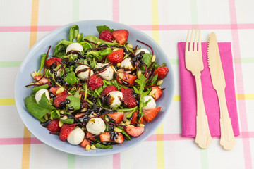 summer salad bowl with strawberries, field salad, beetroot, arugula, mozzarella and pine nuts with balsamic vinegar and cutlery
