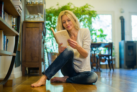 Mature woman relaxing on floor with book at home