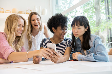 Young women laughing at multimedia smartphone in cafe