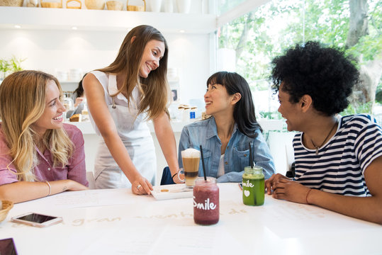 Waitress serving drinks to group of women in cafe