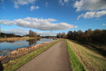 Fototapeta na wymiar Blue sky and big clouds are reflecting in river Rotte with dike and cycle road in Oud Verlaat, Netherlands 