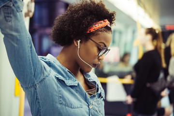 Young African woman listening to music on a subway train